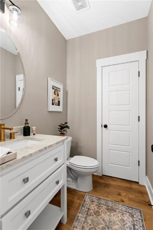 half bathroom featuring visible vents, toilet, wood finished floors, and vanity