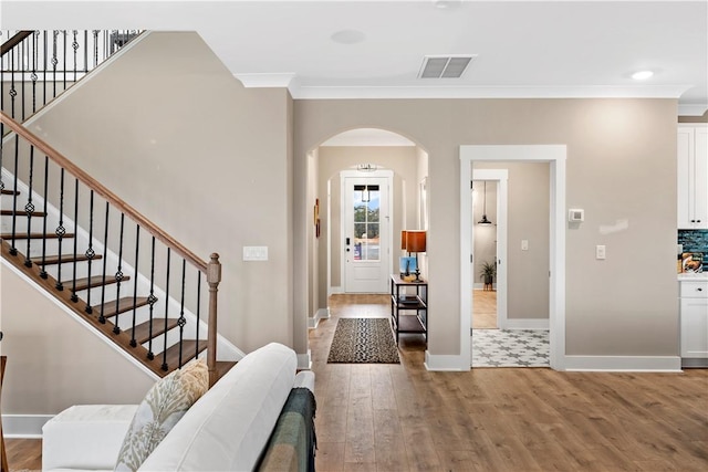 entrance foyer with visible vents, wood finished floors, arched walkways, crown molding, and baseboards