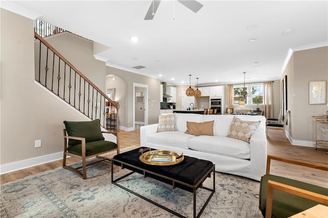 living area featuring light wood-type flooring, stairs, baseboards, and ornamental molding