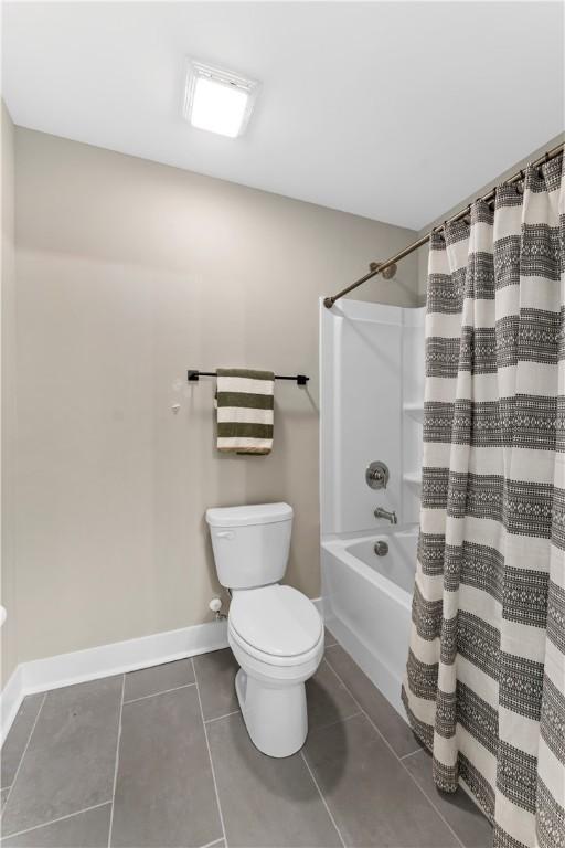 bathroom with baseboards, toilet, shower / bath combination with curtain, and tile patterned flooring