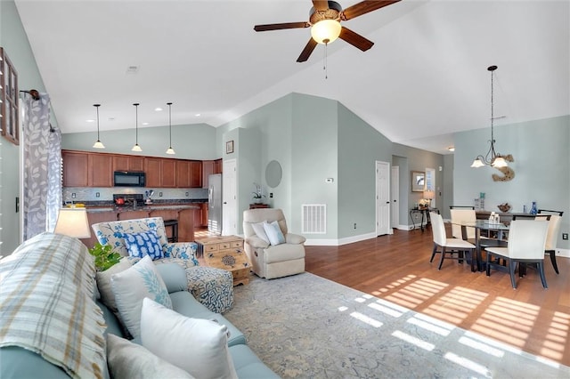 living area with visible vents, high vaulted ceiling, ceiling fan with notable chandelier, wood finished floors, and baseboards