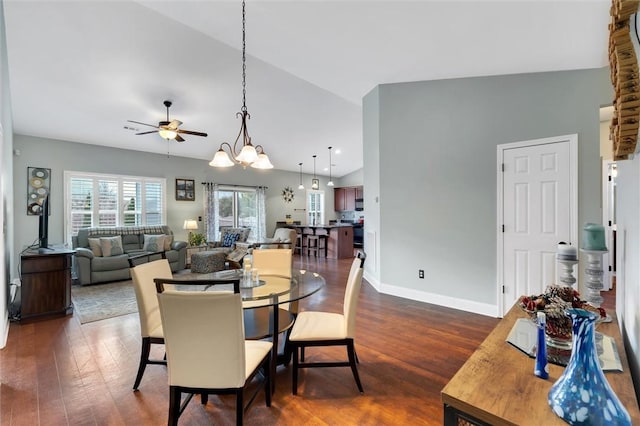 dining area featuring dark wood-style floors, ceiling fan with notable chandelier, baseboards, and vaulted ceiling