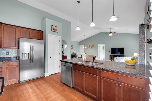 kitchen with a sink, dark stone countertops, stainless steel appliances, light wood-style floors, and hanging light fixtures