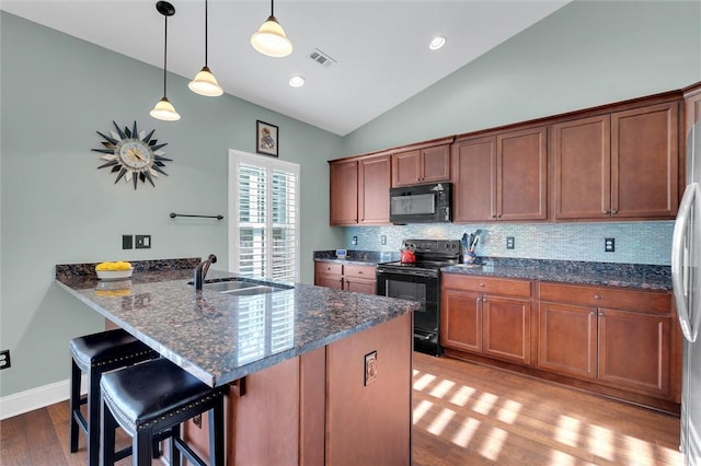 kitchen with visible vents, a sink, black appliances, vaulted ceiling, and a kitchen bar