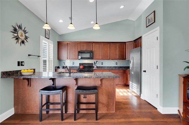 kitchen featuring a breakfast bar area, a peninsula, dark stone counters, dark wood-style flooring, and black appliances