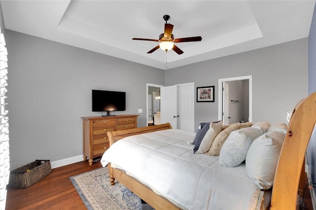 bedroom with dark wood finished floors, a ceiling fan, a raised ceiling, and baseboards