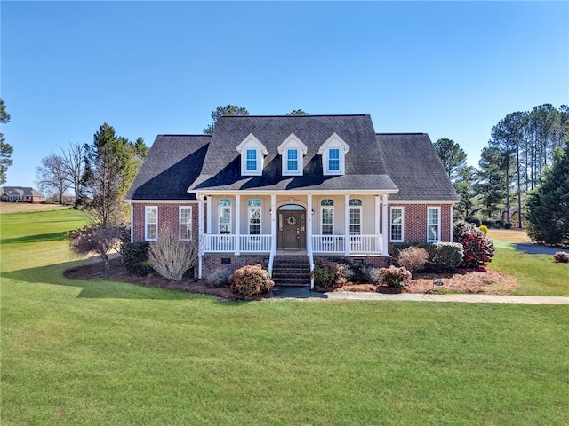 cape cod house featuring brick siding, a porch, a front yard, and roof with shingles