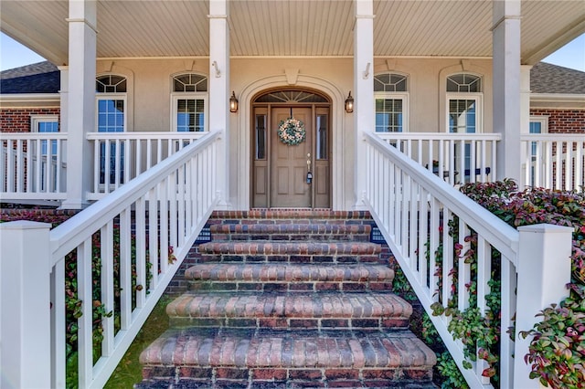 entrance to property featuring stucco siding, brick siding, covered porch, and a shingled roof