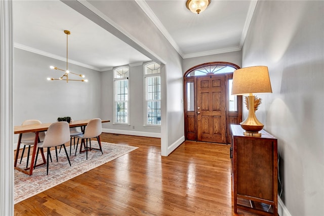 entrance foyer with a chandelier, baseboards, wood finished floors, and crown molding