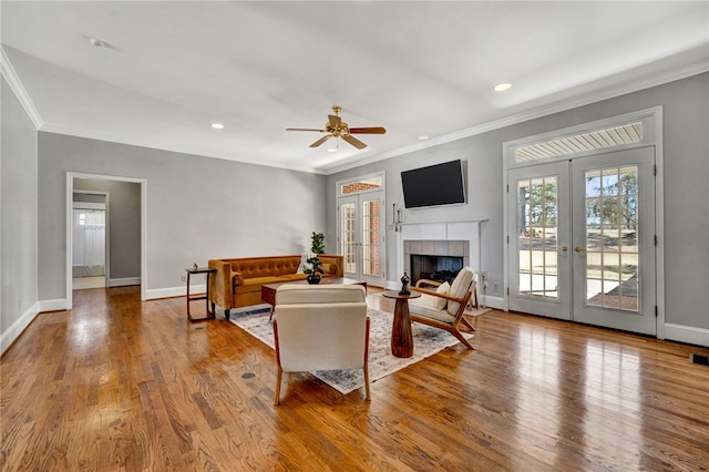 living room featuring baseboards, a tiled fireplace, ornamental molding, french doors, and wood finished floors