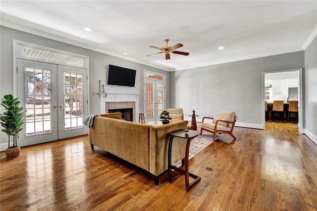 living area with wood finished floors, baseboards, ornamental molding, french doors, and a tiled fireplace