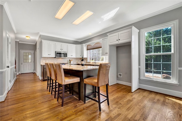 kitchen with a kitchen island, a breakfast bar, light wood-style flooring, stainless steel microwave, and tasteful backsplash