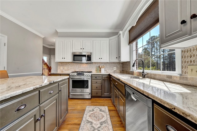 kitchen with light wood-style flooring, ornamental molding, a sink, appliances with stainless steel finishes, and white cabinets