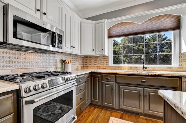 kitchen featuring a sink, stainless steel appliances, dark brown cabinetry, white cabinets, and crown molding