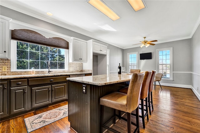 kitchen with white cabinetry, a breakfast bar area, light stone counters, and a sink