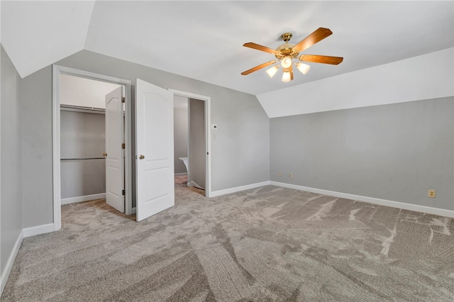 unfurnished bedroom with a walk in closet, baseboards, carpet flooring, and vaulted ceiling