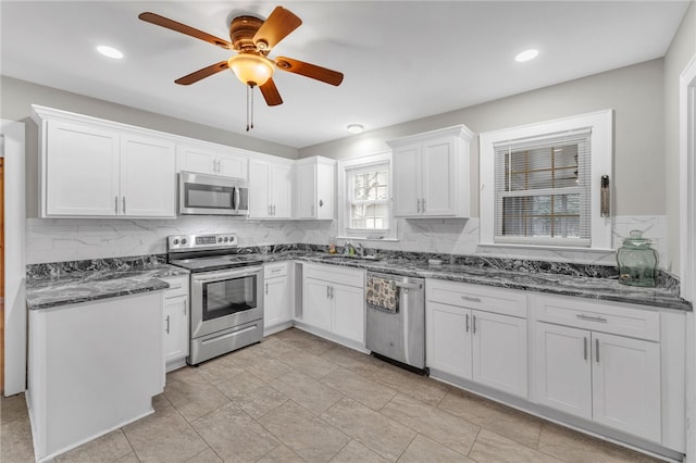 kitchen featuring backsplash, dark stone counters, white cabinets, stainless steel appliances, and a sink