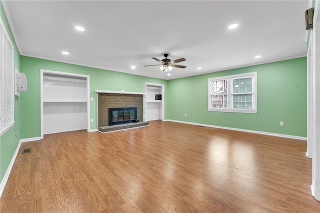 unfurnished living room with visible vents, a ceiling fan, wood finished floors, baseboards, and a brick fireplace