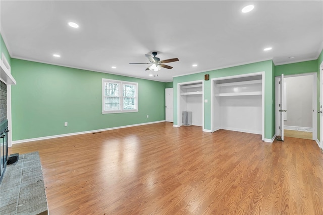 unfurnished living room featuring a ceiling fan, a brick fireplace, light wood-style floors, and ornamental molding