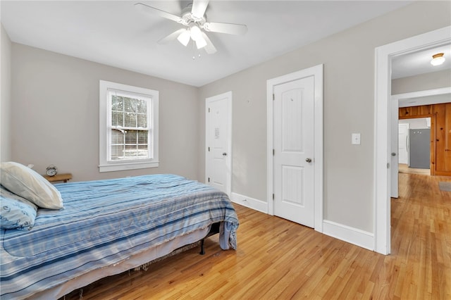 bedroom with light wood-style flooring, a ceiling fan, freestanding refrigerator, and baseboards