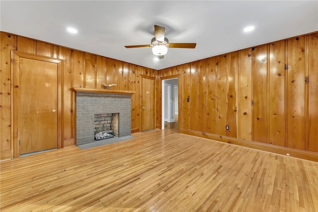 unfurnished living room with a brick fireplace, a ceiling fan, and light wood-style floors