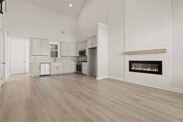 unfurnished living room with visible vents, light wood-style flooring, a sink, a glass covered fireplace, and vaulted ceiling