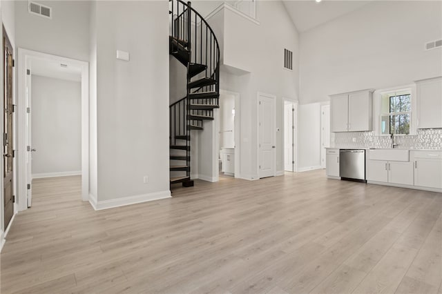 unfurnished living room featuring visible vents, stairway, light wood-type flooring, and a sink