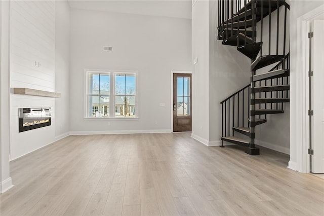 unfurnished living room featuring stairs, light wood-type flooring, visible vents, and a large fireplace