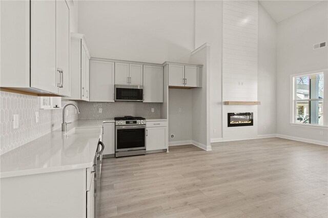 kitchen featuring visible vents, light countertops, appliances with stainless steel finishes, a high ceiling, and a sink