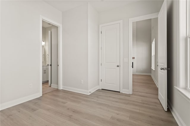 unfurnished bedroom featuring light wood-type flooring, baseboards, and ensuite bathroom