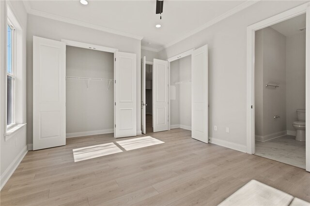 unfurnished bedroom featuring two closets, light wood-style flooring, ensuite bath, crown molding, and baseboards