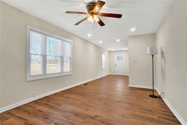 empty room with a ceiling fan, visible vents, wood finished floors, baseboards, and recessed lighting