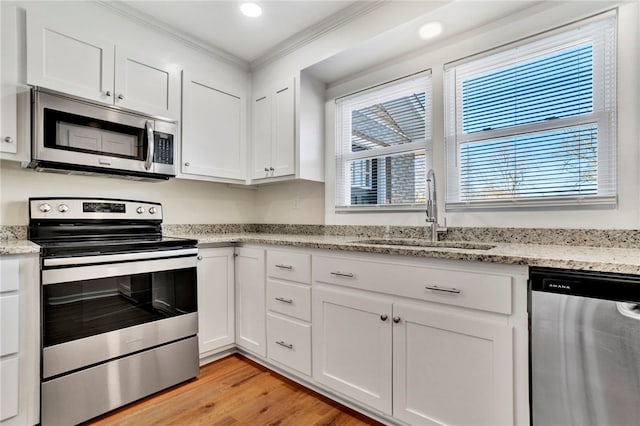 kitchen featuring light wood finished floors, ornamental molding, appliances with stainless steel finishes, white cabinets, and a sink