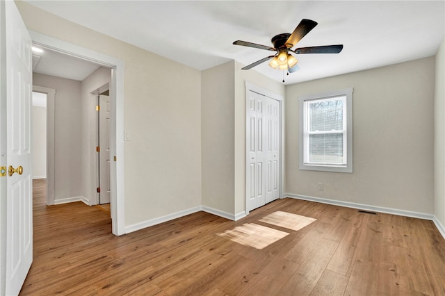 unfurnished bedroom featuring a closet, baseboards, light wood-style floors, and ceiling fan