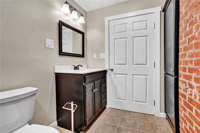 bathroom with tile patterned floors, toilet, brick wall, and vanity