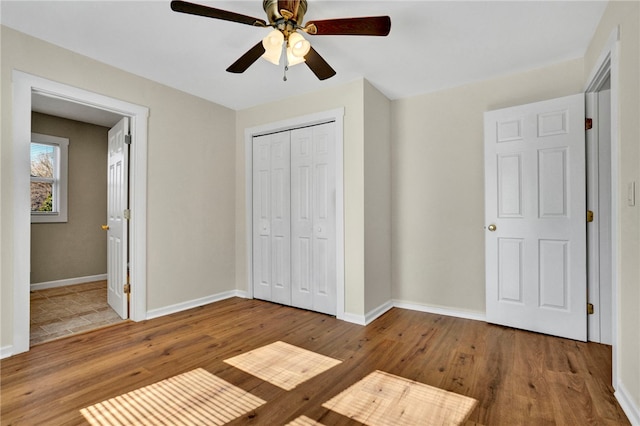 unfurnished bedroom featuring wood finished floors, baseboards, ensuite bath, ceiling fan, and a closet