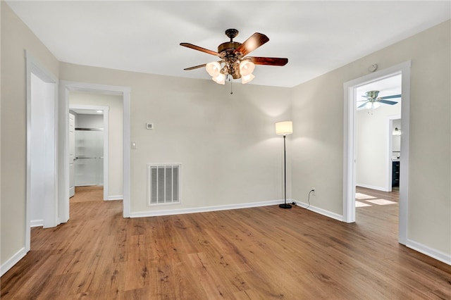 empty room with visible vents, a ceiling fan, baseboards, and wood finished floors