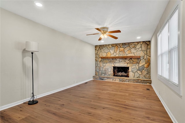 unfurnished living room with a stone fireplace, wood finished floors, baseboards, and ceiling fan