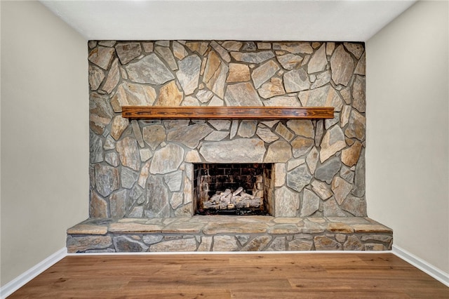 interior details with a stone fireplace, wood finished floors, and baseboards