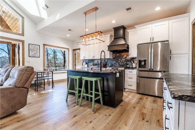 kitchen featuring a breakfast bar area, custom exhaust hood, stainless steel refrigerator with ice dispenser, open floor plan, and backsplash