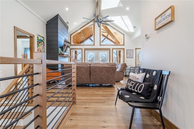 interior space with high vaulted ceiling, a skylight, ceiling fan, an upstairs landing, and light wood-type flooring