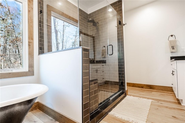 full bathroom with a shower stall, a freestanding tub, wood finished floors, and baseboards