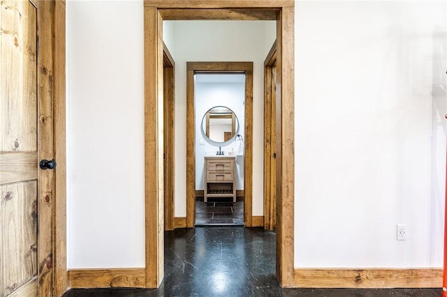 corridor featuring finished concrete floors, baseboards, and a sink