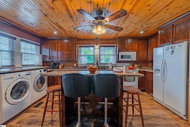 kitchen featuring light wood finished floors, a center island, washing machine and dryer, a kitchen breakfast bar, and white appliances