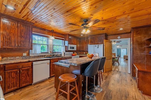 kitchen with white appliances, a sink, light wood-style floors, a kitchen breakfast bar, and a center island