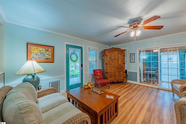 living room with light wood-type flooring, ornamental molding, and a ceiling fan