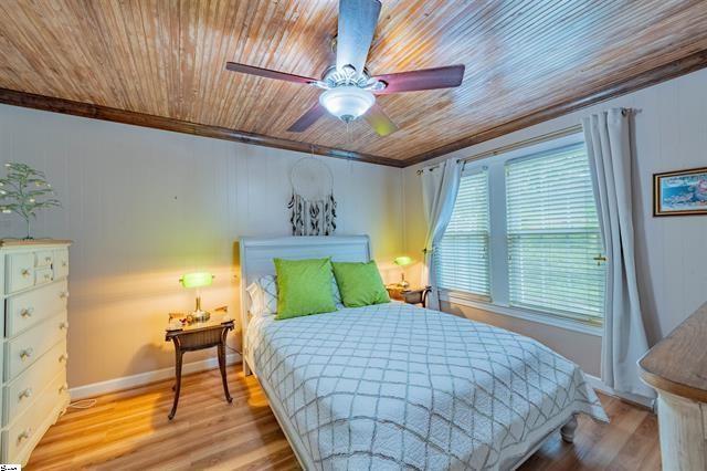 bedroom with baseboards, wood ceiling, wood finished floors, and ornamental molding