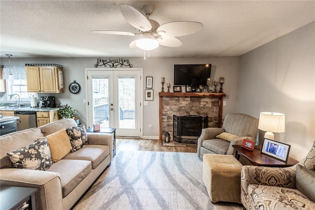 living room with light wood finished floors, a fireplace, ceiling fan, french doors, and a textured ceiling