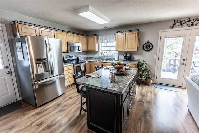 kitchen featuring a textured ceiling, light wood finished floors, light brown cabinetry, and stainless steel appliances