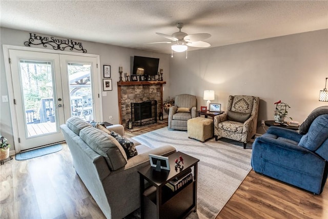 living area featuring wood finished floors, ceiling fan, a stone fireplace, french doors, and a textured ceiling